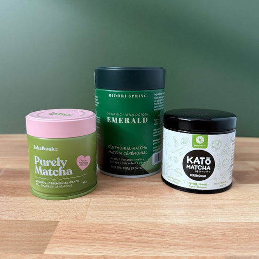 Three containers of matcha tea on a wooden surface with a green background